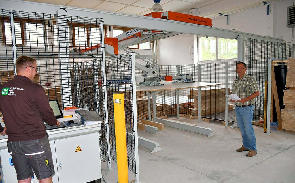 Die neue Maschine nimmt in der Halle in Klietz fast den gesamten Platz ein. Sie steht ?hinter Gittern?, zudem schützen Lichtschranken die Arbeiter, sollten sie zu dicht an die Maschine kommen. Möbelbauer Manuel Graf (links) hat einen dreiwöchigen Lehrgang zum Umgang mit der Maschine hinter sich. Tilo Bolle (rechts) freut sich, wenn die Produktion damit demnächst starten kann.