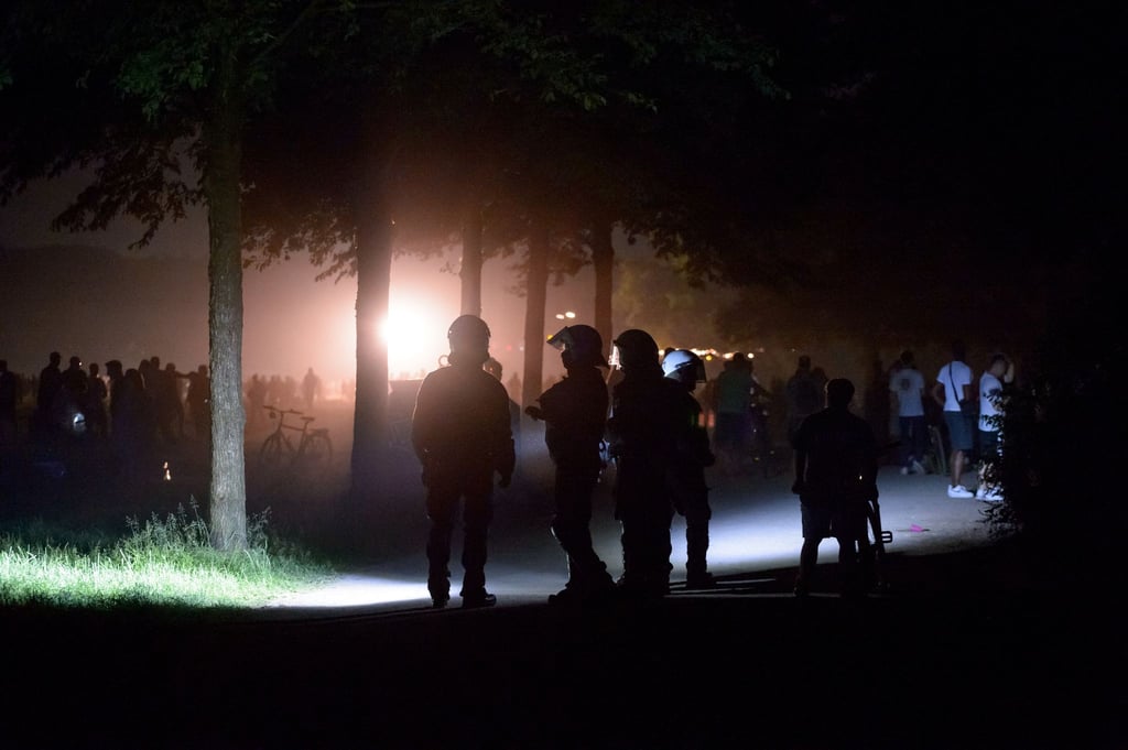 Behelmte Polizisten stehen am Rande der Stadtpark-Wiese und werden von einem Lichtmast angestrahlt. Die Polizei hat eine Party mit rund 3000 Menschen im Hamburger Stadtpark aufgelöst.