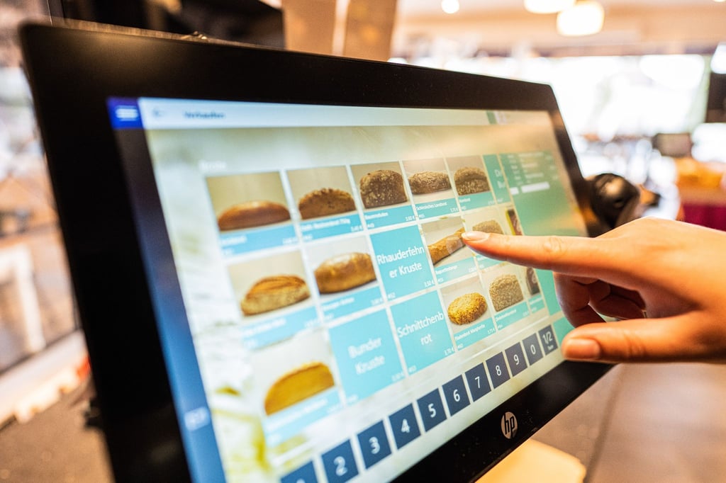 Eine Verkäuferin einer Bäckerei tippt am Kassenbildschirm auf die Abbildung eines Brotes, das verkauft werden soll. (Archivbild)