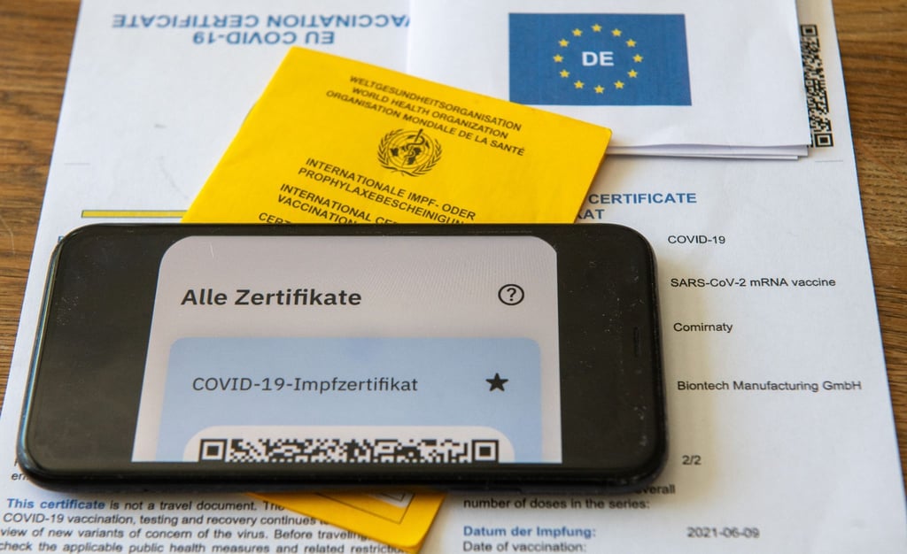 Ein Impfpass und ein Smartphone, auf dem die App CovPass läuft, liegen auf einem Impfzertifikat, das von einer Apotheke ausgestellt wurde.