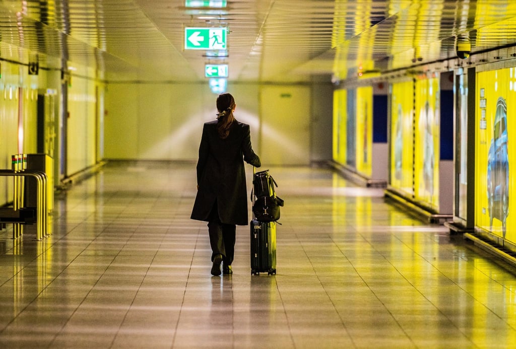 Eine Frau geht mit ihrem Koffer durch einen leeren gang am Flughafen.