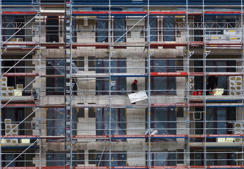 Zwei Arbeiter auf einem Gerüst von einem Rohbau auf einer Baustelle.