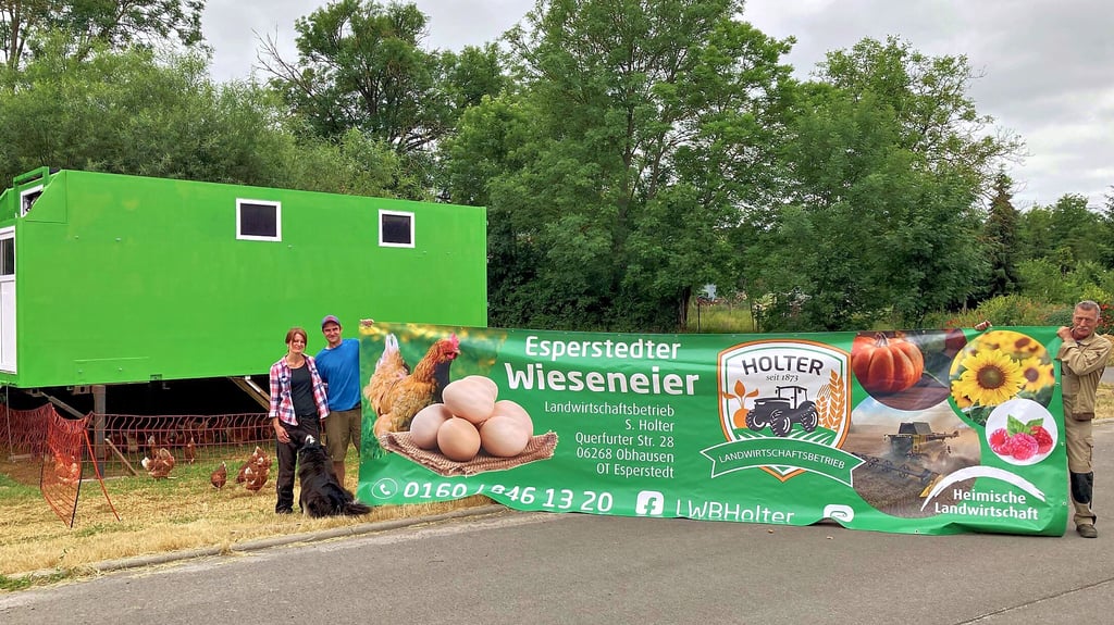 Susanne Holter, ihr Lebensgefährte Erik Seydel und ihr Vater Heinrich Holter mit einem Banner, das am mobilen Hühnerstall angebracht werden soll.