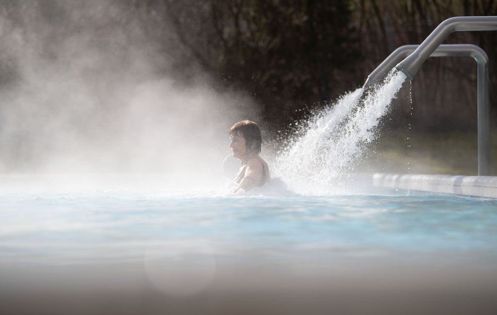 Eine Besucherin einer Therma steht unter einem Wasserstrahl.