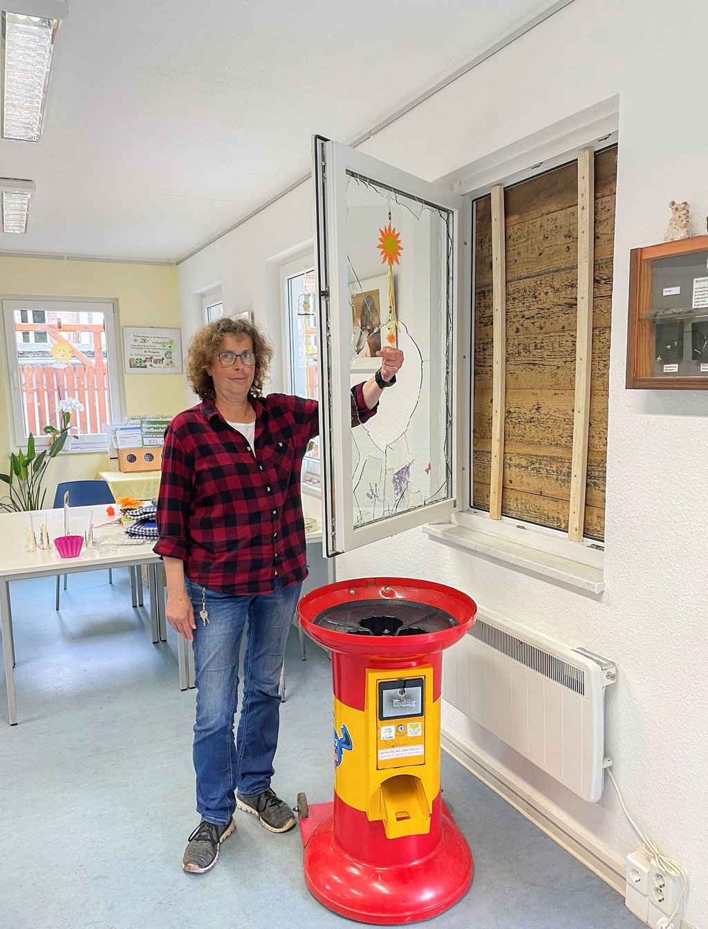 Heimatnaturgarten-Chefin Ute Radestock steht an dem zerschlagenen Fenster. Es ist nach dem Einbruch notdürftig mit Brettern gesichert worden. Vor ihr steht der von den Einbrechern zerstörte Spielzeugautomat.