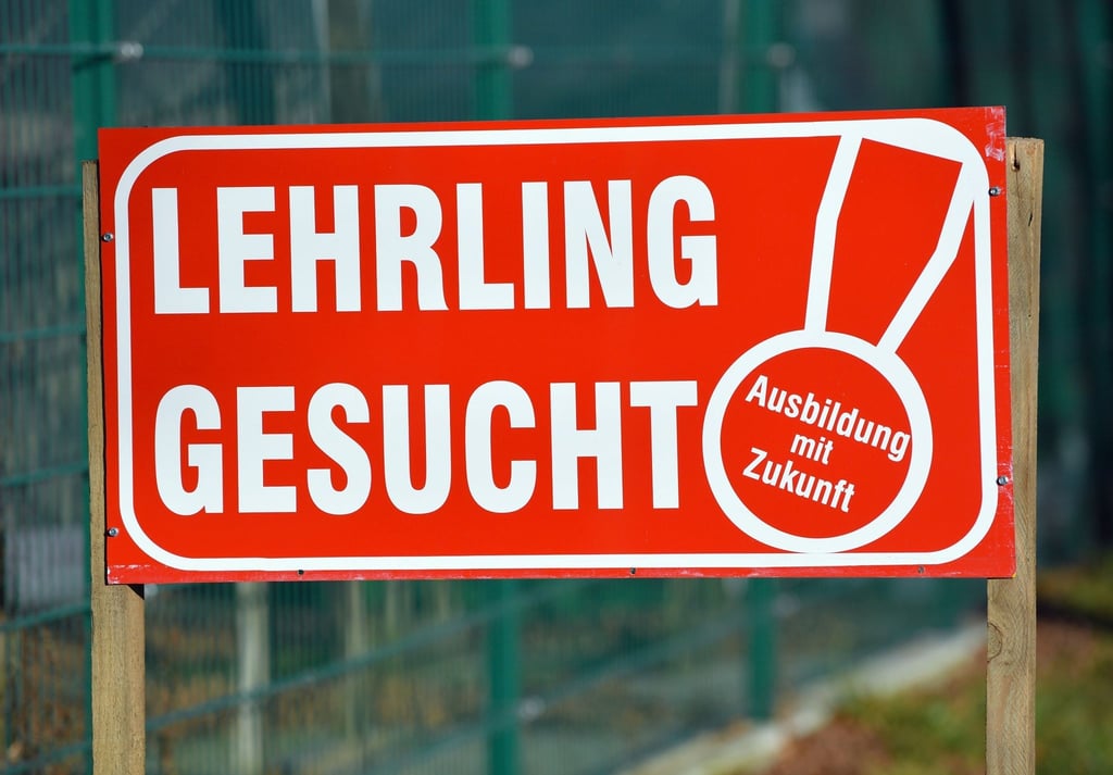 Ein Schild mit „Lehrling gesucht Ausbildung mit Zukunft“ ist vor einem Zaun aufgestellt.