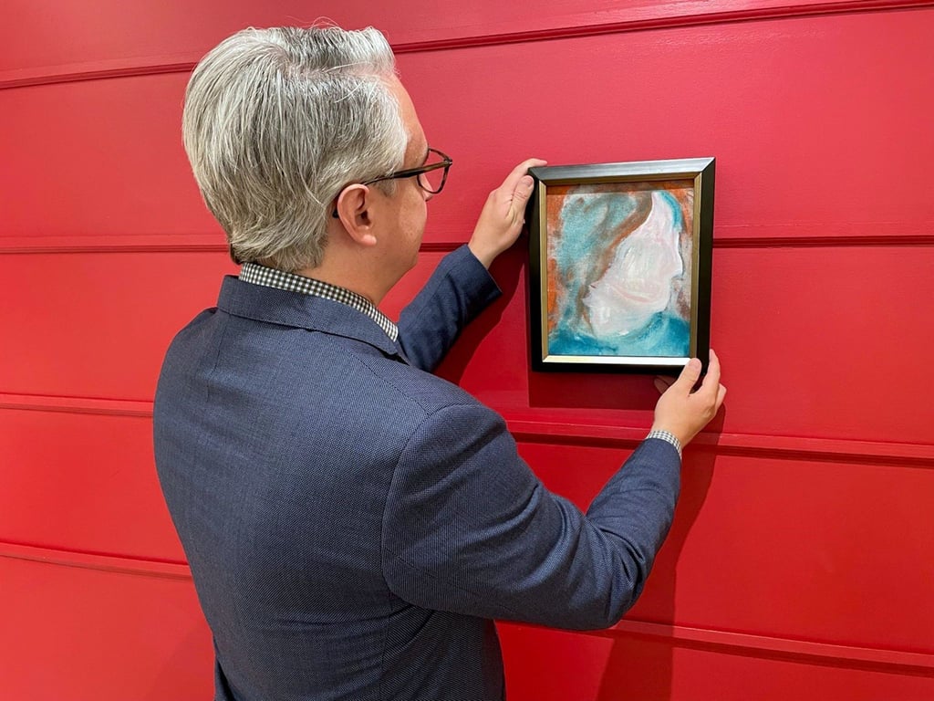 Rob Cowley, Präsident & Senior Spezialist bei Cowley Abbott, hängt ein zufällig in einem Spendenzentrum für Haushaltsgegenstände entdecktes Gemälde von Musik-Legende David Bowie (1947-2016) an die Wand.