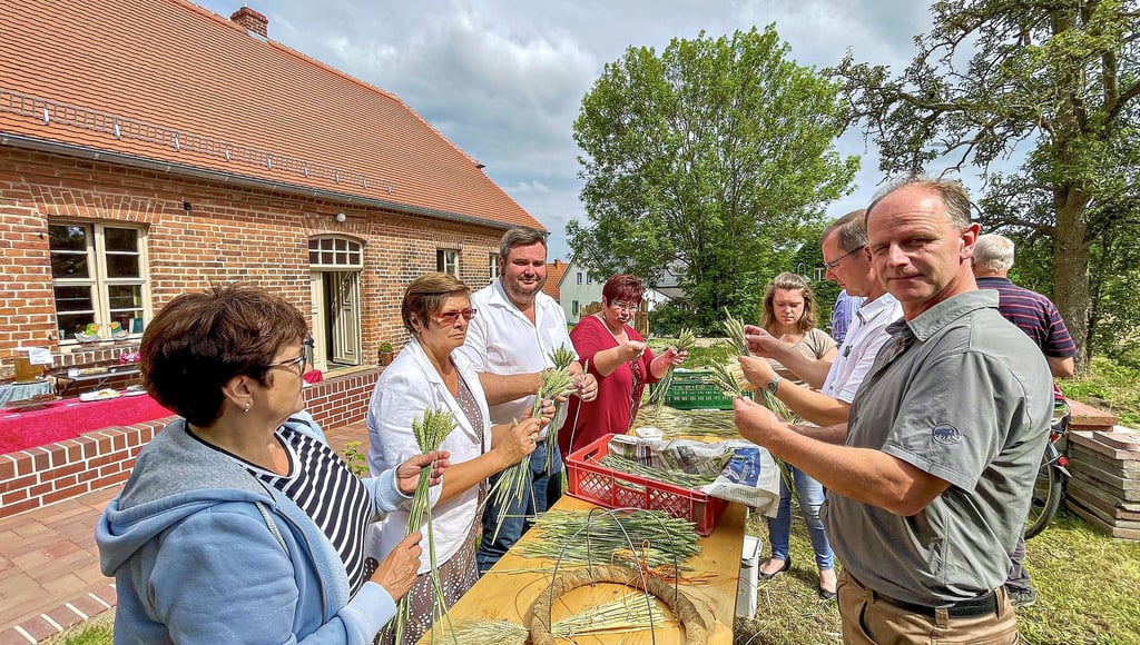 Nach dem Motto „Viele Hände, schnelles Ende“ haben Teilnehmer vor der sanierten Dorfschule in Meuro beim Bau einer Erntekrone geholfen.