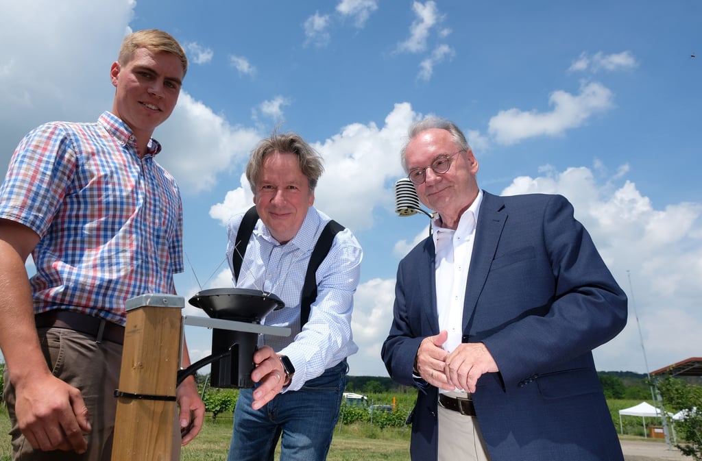 Winzer Lukas Herzer (v.l.n.r.), Meteorologe Jörg Kachelmann sowie Reiner Haseloff (CDU) stehen am Regenmesser einer Wetterstation. In einem Weinberg der Anbauregion Saale-Unstrut wurde eine neue Messeinrichtung in Betrieb genommen