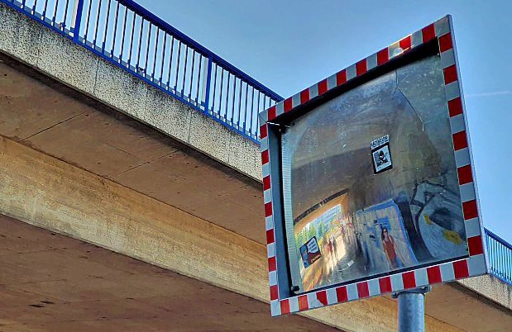 Ein Verkehrsspiegel am Fuß- und Radweg, der an der Tunnelbaustelle in Magdeburg und unter der Rinbrücke entlangführt. Aufkleber und Beschlag behindern den Blick.