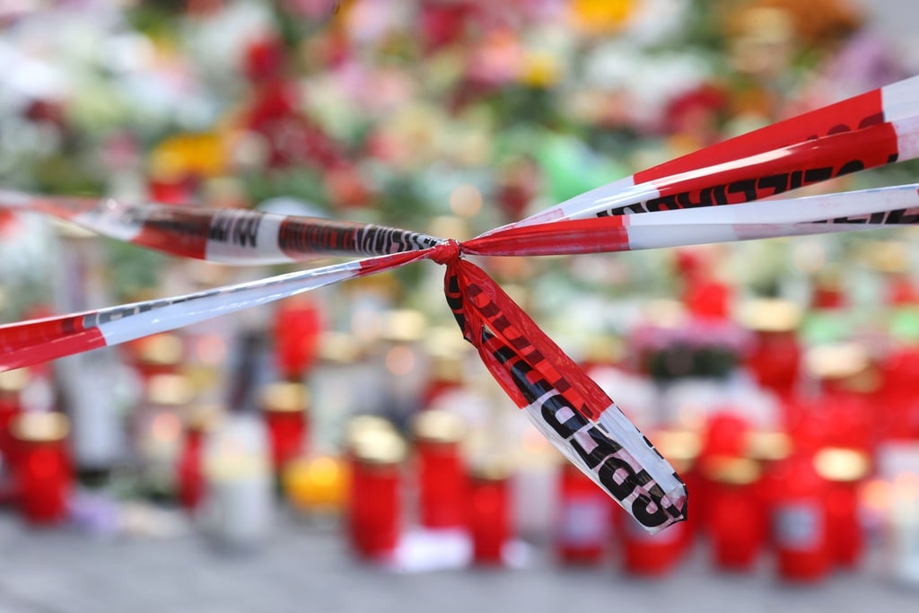 Blumen und Kerzen stehen vor dem abgesperrten Kaufhaus in Würzburg, in dem ein Mann Menschen mit einem Messer attackiert hatte.