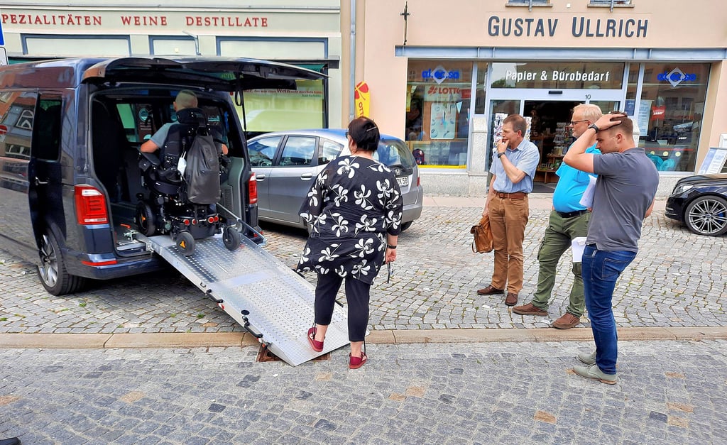 Tilman Altenberger (von links) verlässt mit seinem Rollstuhl über eine Heckklappe das Auto, während seine Mutter und die Vertreter der Stadt: Georg-Wilhelm Westrum (Leiter Bauamt), Michael Genz (Tiefbauamt) sowie Philipp Krüger (Pressesprecher) den Vorgang am Markt in Stendal beobachten.