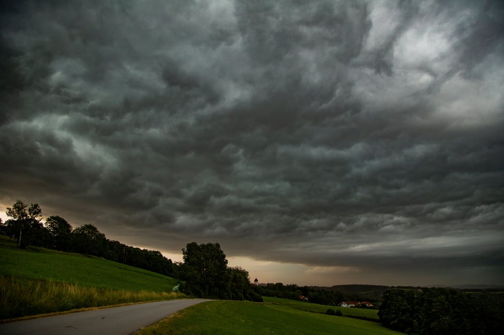 Dunkle Gewitterwolken sind am Nachthimmel über einer Wiese zu sehen.
