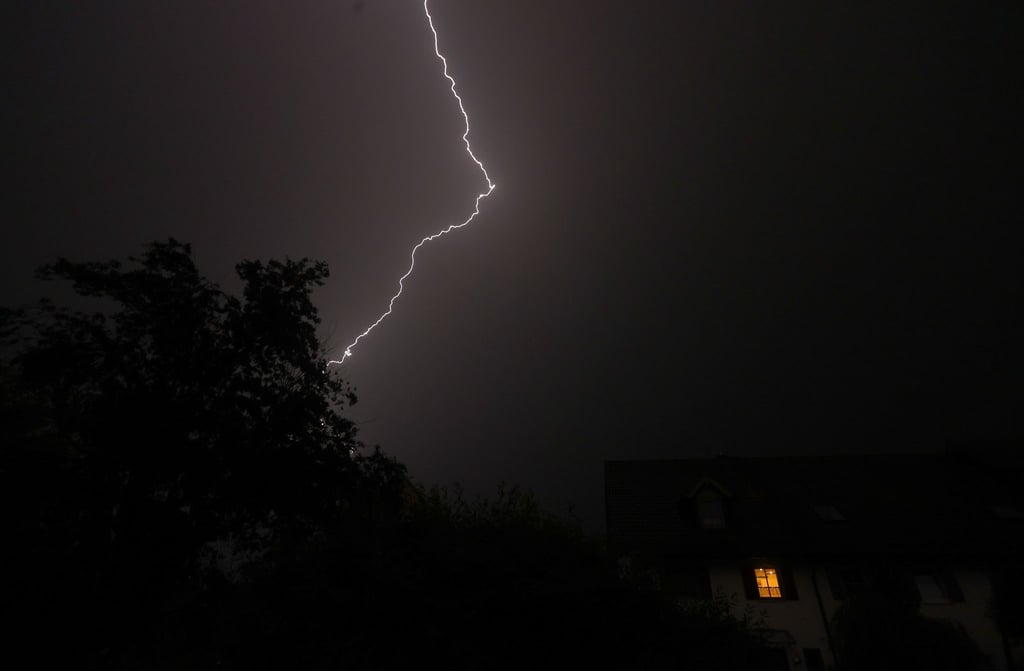 Ein Blitz entlädt sich am Nachthimmel über Reihenhäusern.