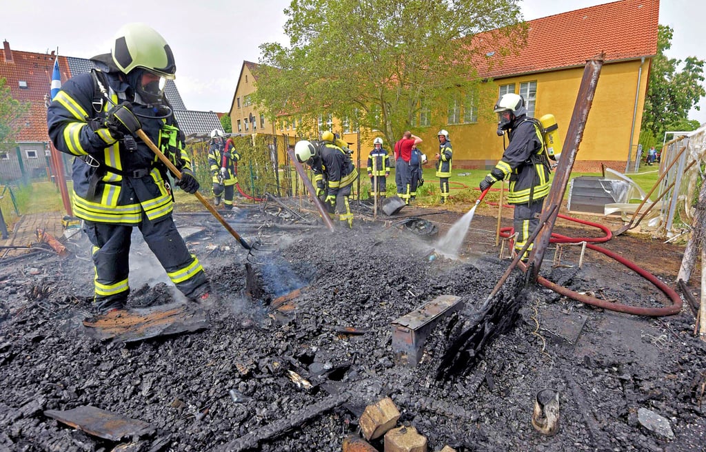 Einsatz in Nachterstedt: Feuerwehrleute mit Atemschutzmaske ziehen am Ende verkohlte Bretter auseinander und löschen letzte Glutnester.