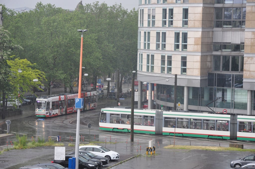 Zwei Straßenbahnen fahren auf den Gleisen in der regennassen Fahrbahn am City Carré in Magdeburg.