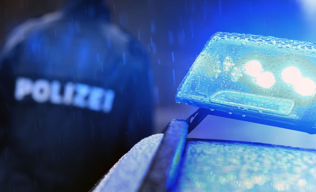 Ein Polizist steht vor einem Streifenwagen mit Blaulicht.