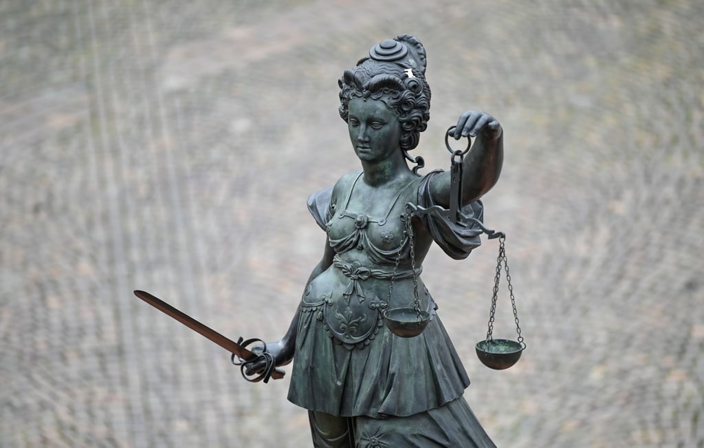 Eine Bronzefigur der Justitia steht mit Waage und Schwert in den Händen auf einem Brunnen.