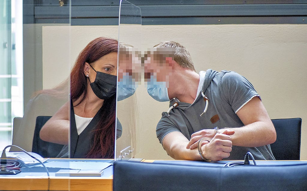 Der Beschuldigte berät sich mit seiner Verteidigerin. Beide sind durch eine Plexiglasscheibe getrennt.
