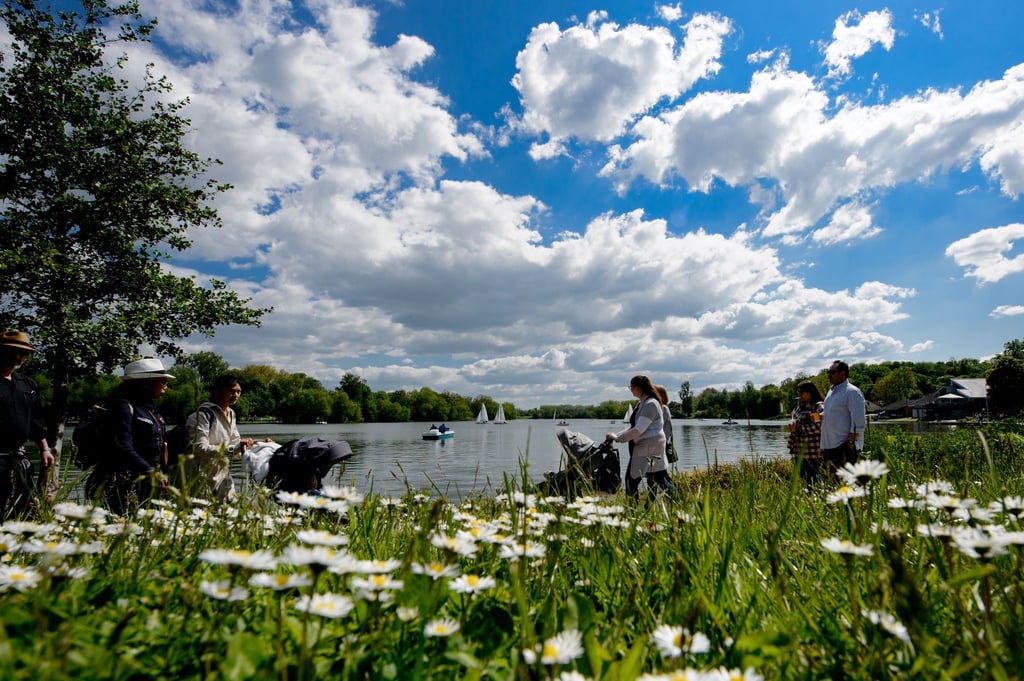 Spaziergänger gehen bei sommerlichem Wetter um den Kiessee, auf dem Boote unterwegs sind.