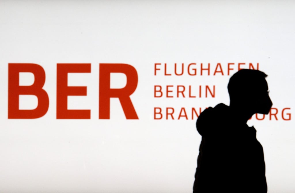 Ein Mann geht im Terminal 1 des Flughafens Berlin Brandenburg an dem erleuchteten Logo BER vorbei.