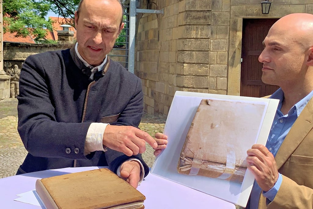 Restaurator Nikolai Exner (links) erläutert in Halberstadt die Besonderheiten bei der Restaurierung des Fremdenbuches des Ströbecker Schachvereins. Der neue Sammlungsleiter für das Schachmuseum Ströbeck, Cihangir Erol, zeigt Fotos vom Ausgangszustand des Buches.
