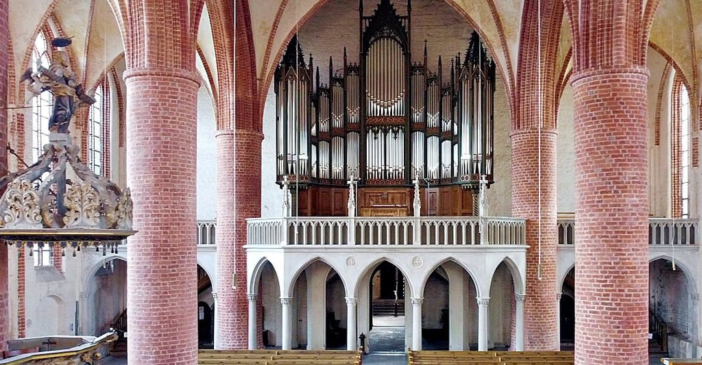 Die Altarrahmung fällt in die Epoche des Baus von Orgel und Empore. Deshalb die Ähnlichkeit bei den gotischen Bögen in Groß und in Klein.
