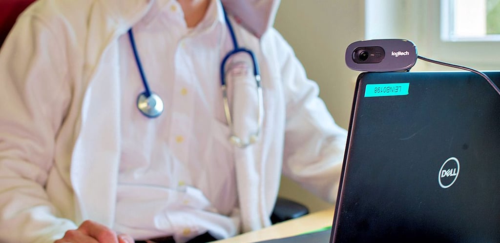 Ein Hausarzt spricht während einer Videosprechstunde in seiner Praxis mit einer Patientin.