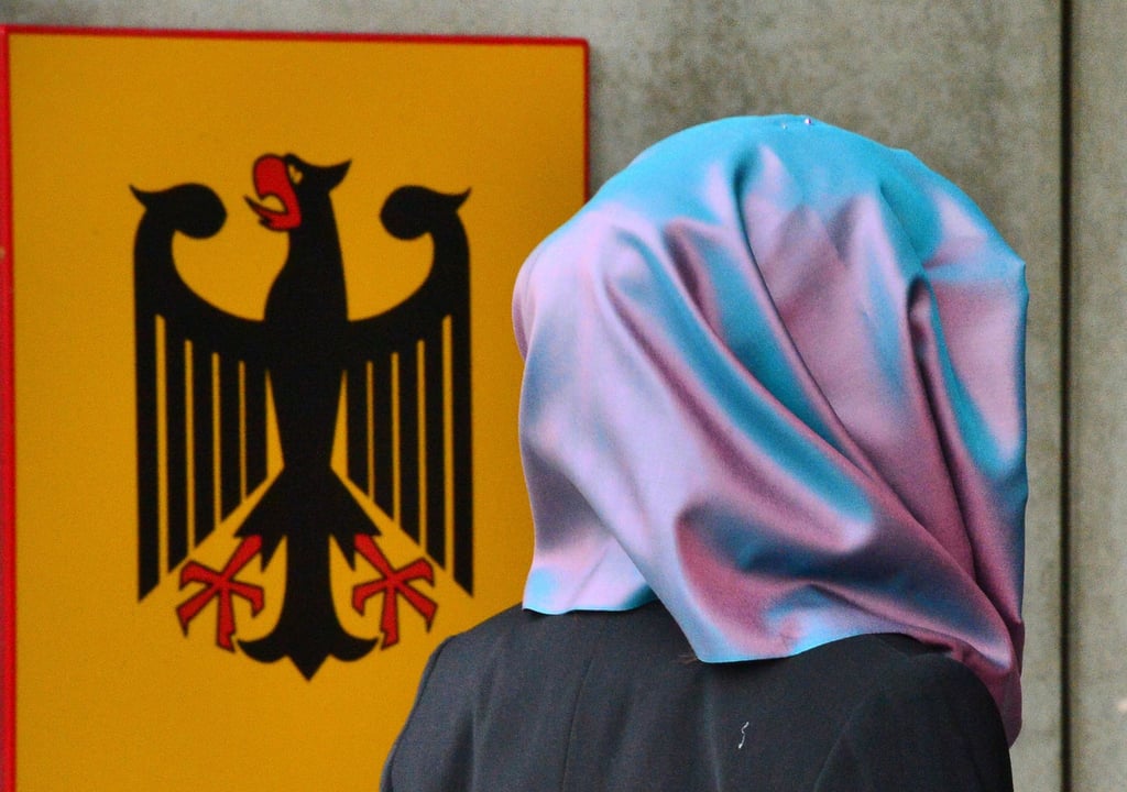 Eine junge Frau mit Kopftuch geht an einem Behördenschild mit dem Bundesadler vorbei.