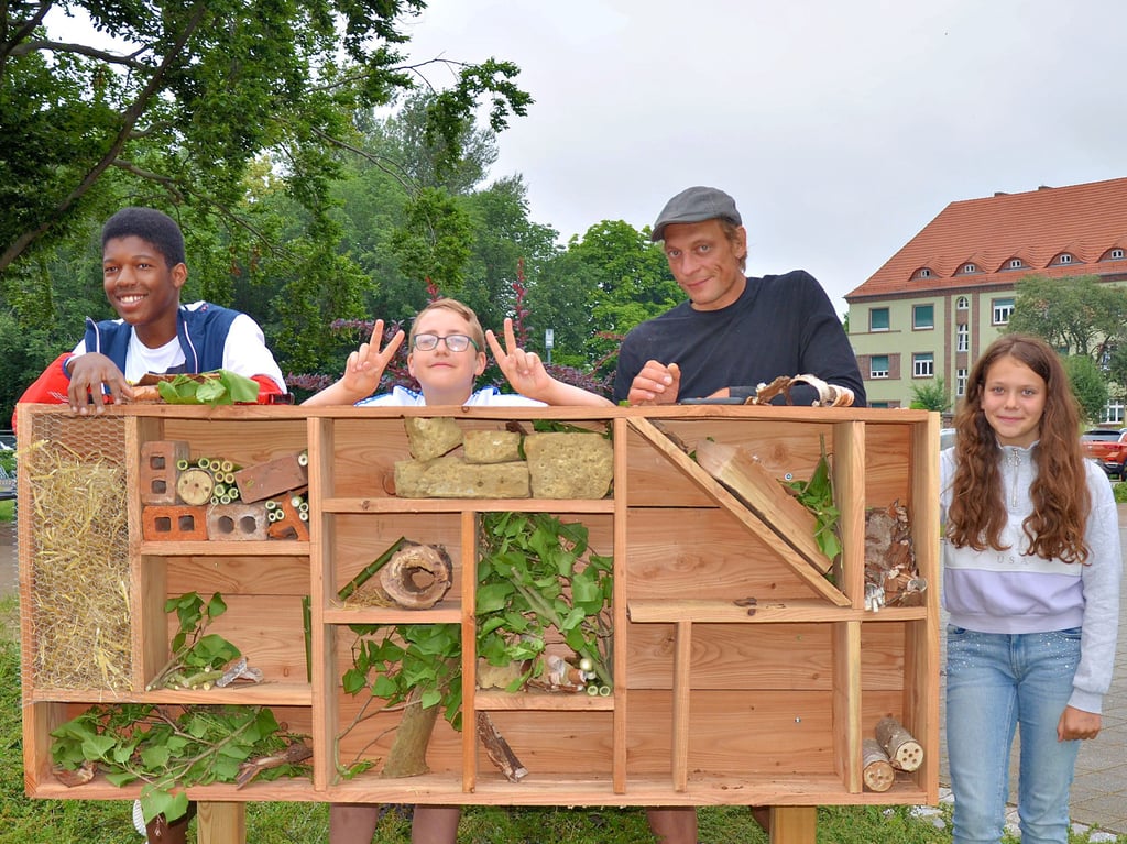 Drei der neun Schüler der Projektgruppe der Comenius-Sekundarschule Stendal präsentieren mit Marco Dörheit das Insektenhotel. Einige Fächer des Holzbaus werden noch mit Naturmaterialien ausgefüllt.