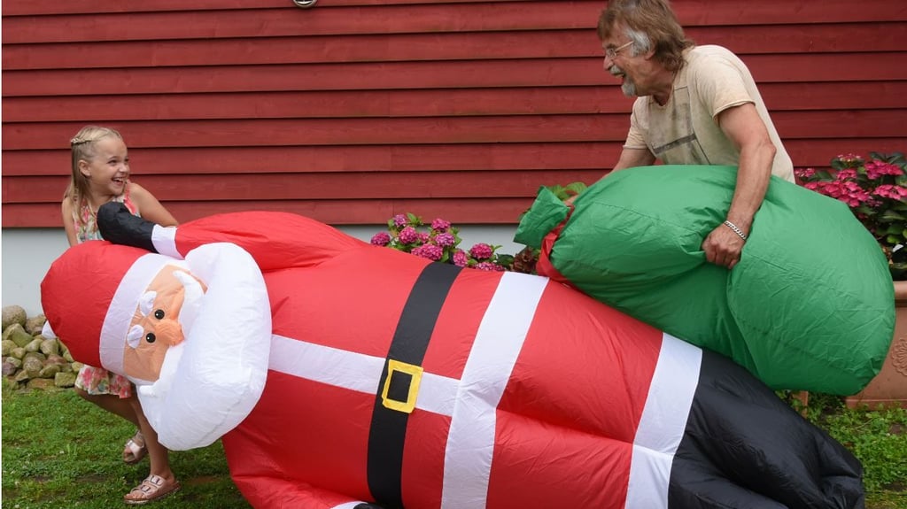 Lachend tragen Alicia und ihr Opa Dietmar Sawatzke den drei Meter großen aufgeblasenen Weihnachtsmann neben die mit Sommerblumen dekorierte Eingangstür.