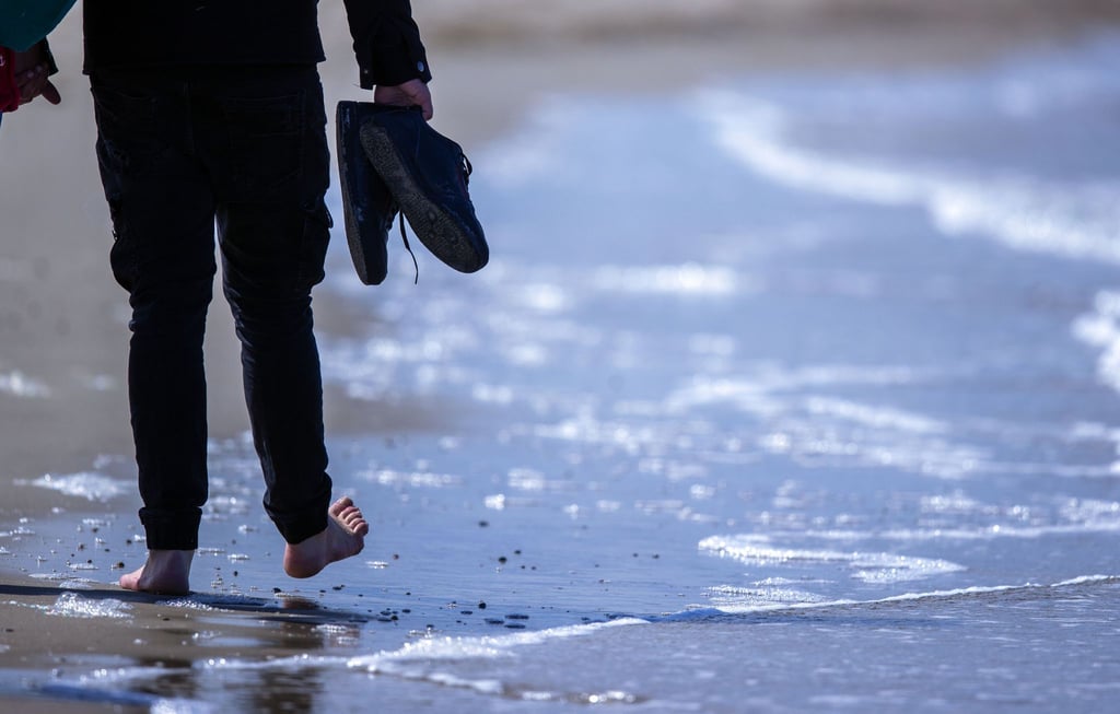 Barfuß geht ein Mann am Strand von Warnemünde durch das Wasser der Ostsee.