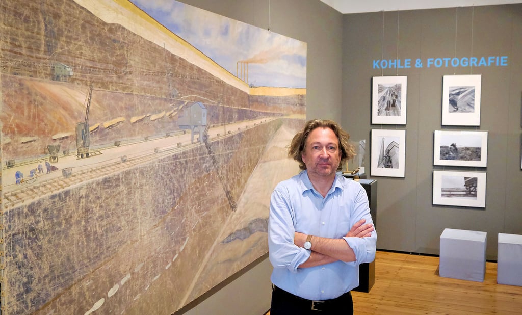 Universitätskustos Dirk Schaal steht in der neuen Ausstellung vor einem Bild, das die Kohleförderung in der Grube Cäcilie im Geiseltal zeigt.