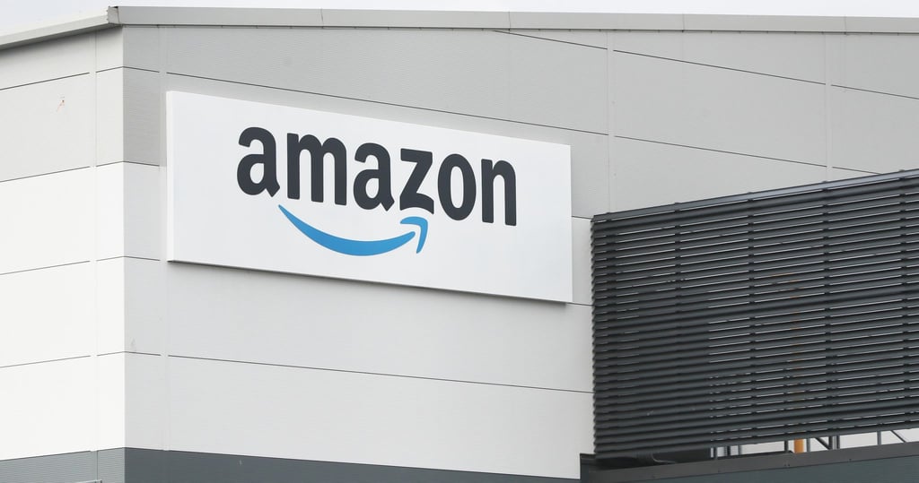Eine Tafel mit dem Logo des Onlineversandhändlers Amazon ist an der Fassade eines Amazon-Warenlagers angebracht.