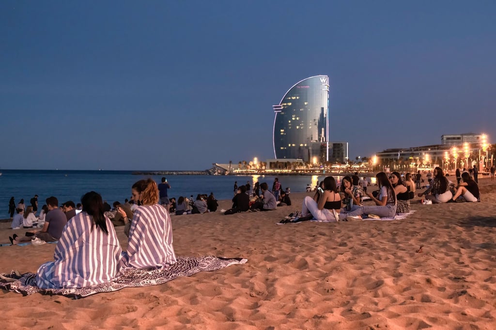Junge Menschen sitzen in Barcelona, Katalonien, mit Abstand voneinander am Strand.