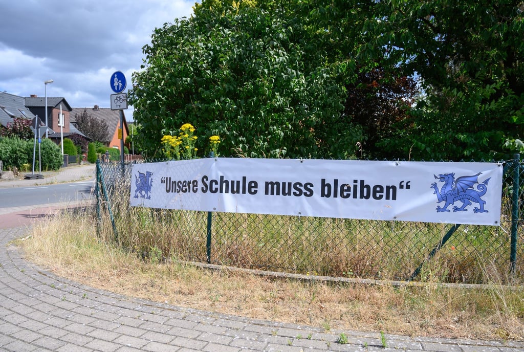 An einer Straße hängt ein Transparent mit der Aufschrift „Unsere Schule muss bleiben“.