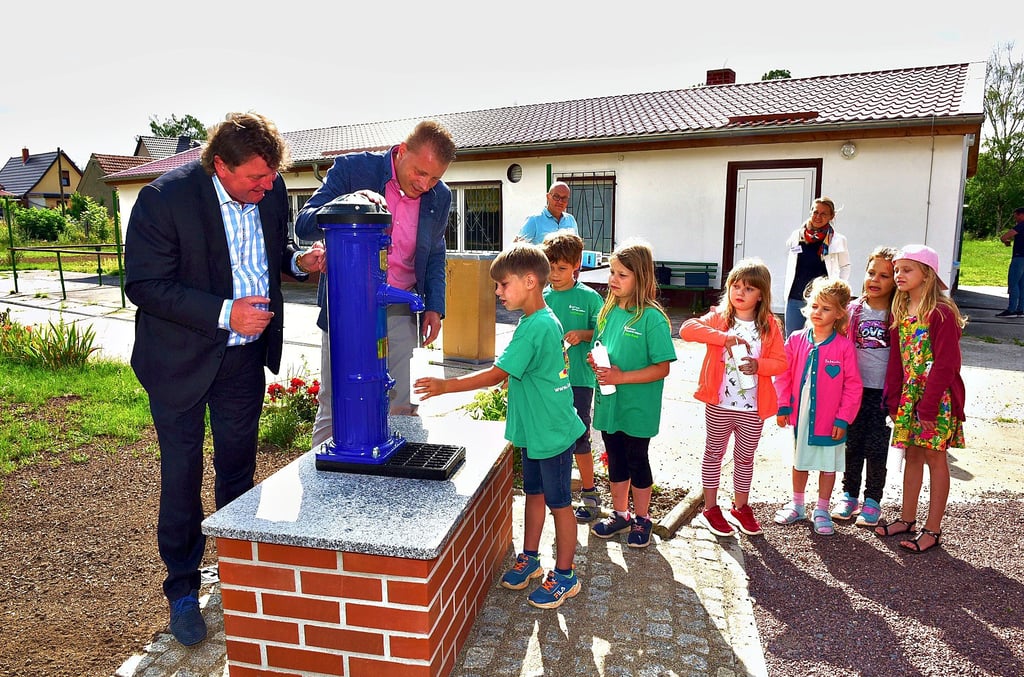 Midewa-Chef Uwe Störzner und Eislebens Bürgermeister Carsten Staub (v.li.) nehmen gemeinsam mit den Kindern der Kita „Gänseblümchen“ den Trinkbrunnen im Ortsteil Osterhausen in Betrieb.
