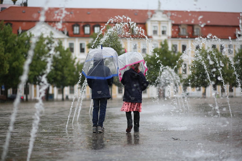 Zwei Kinder geht mit Schirmen bei Regenwetter durch ein Wasserspiel auf dem Domplatz.