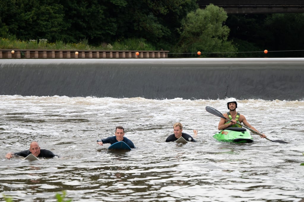 Surfer und ein Kayakfahrer fahren an dem Wehr, an dem die Surfwelle entstehen soll.