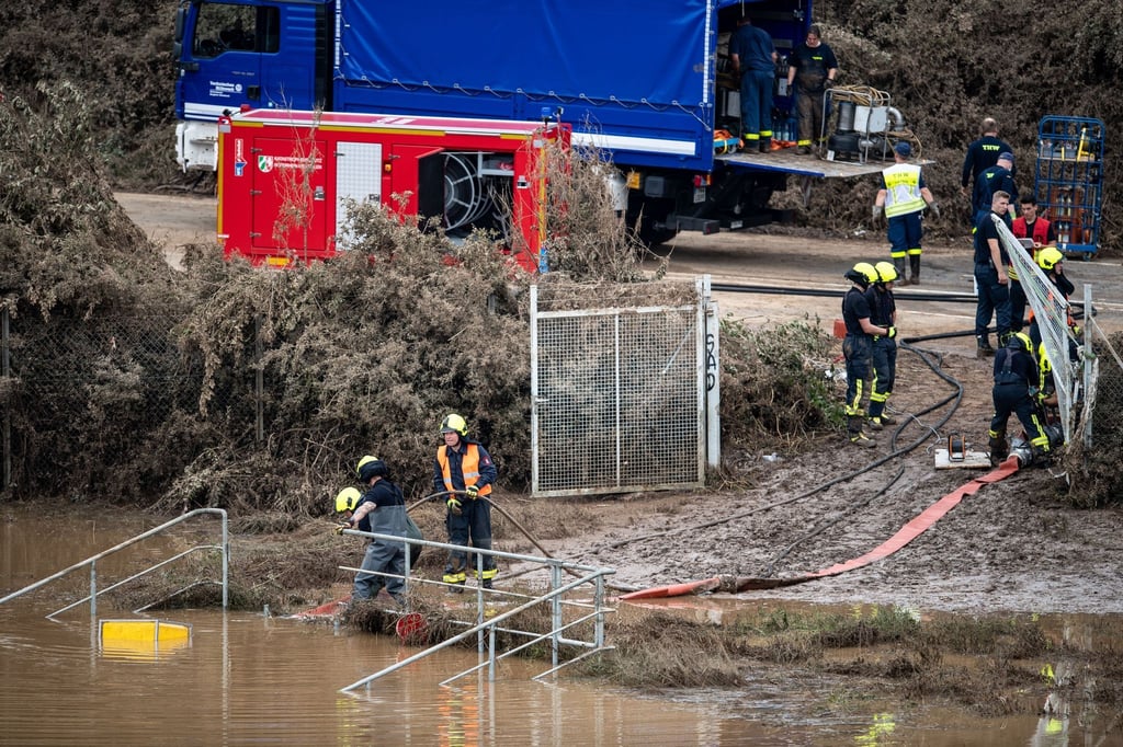Helfer von Feuerwehr und Technischem Hilfswerk (THW) pumpen Wasser aus einem Regenrückhaltebecken ab, in dem sich noch Fahrzeuge befinden sollen.