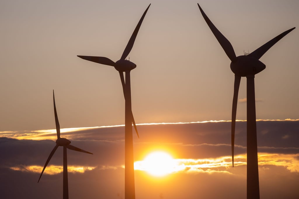 Die Sonne geht hinter Windkraftanlagen unter.