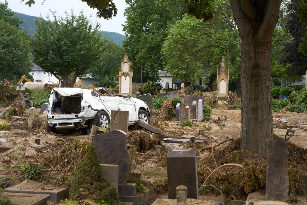 Ein Auto, das bei der Hochwasserkatastrophe auf den Friedhof von Hannover Ahrweiler geschwemmt worden ist, steht auf einem Grabfeld. Der Friedhof ist total verwüstet.