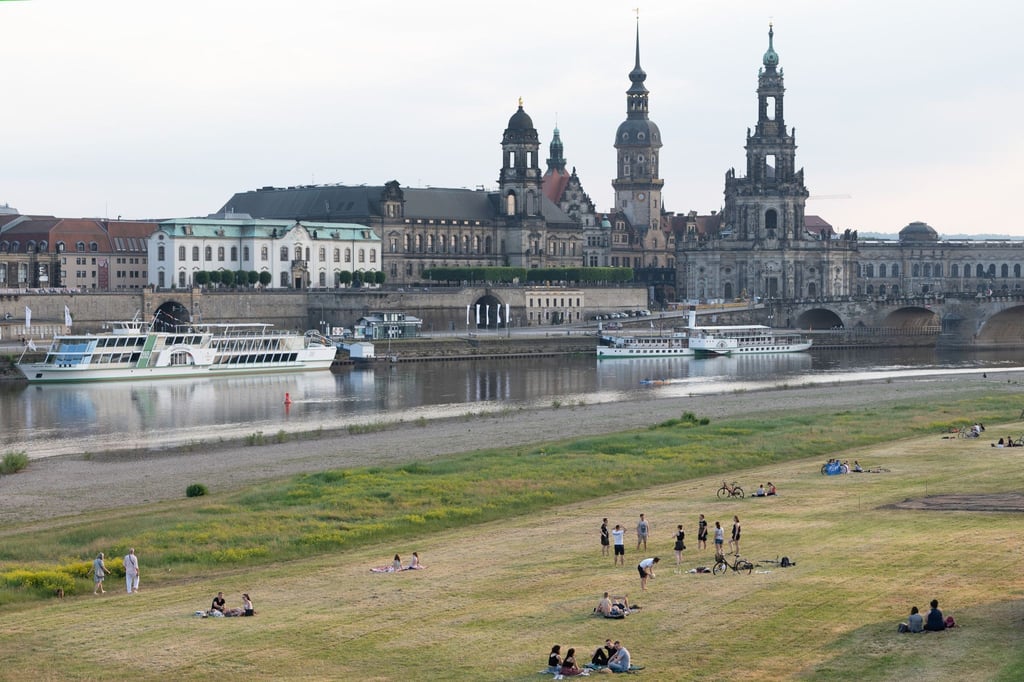 Menschen sitzen und stehen bei warmem Wetter am Ufer der Elbe vor der Kulisse der Altstadt.