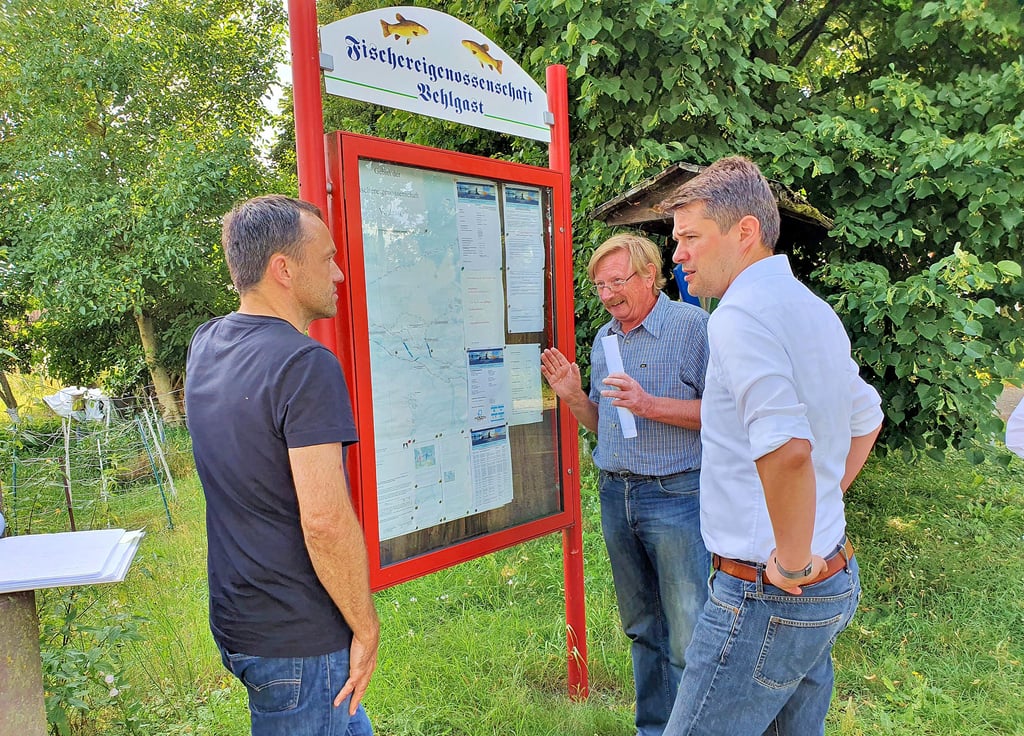 Marcus Faber nimmt zusammen mit Wilfried Ebert und Daniel Bloch (von rechts) am Vehlgaster Ortseingang die Informationstafel der Fischereigenossenschaft des Haveldorfes in Augenschein.
