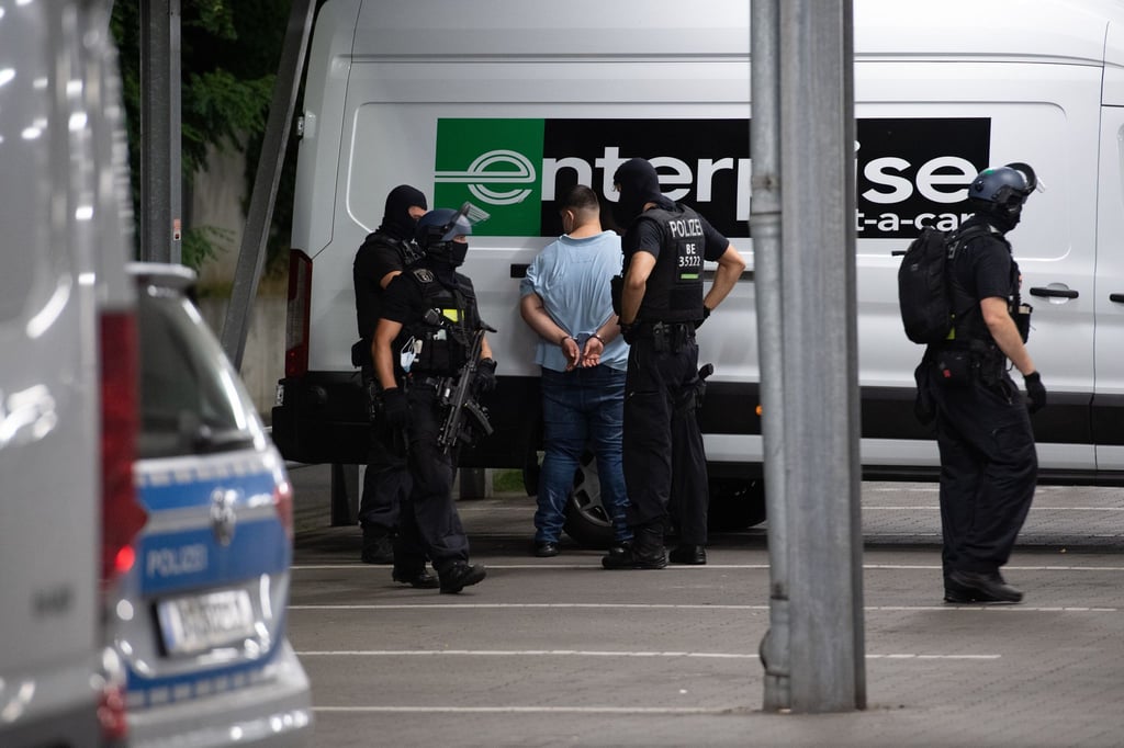Polizisten stehen nach dessen Festnahme neben einem Taterdächtigen auf dem Gelände eines Baumarktes.