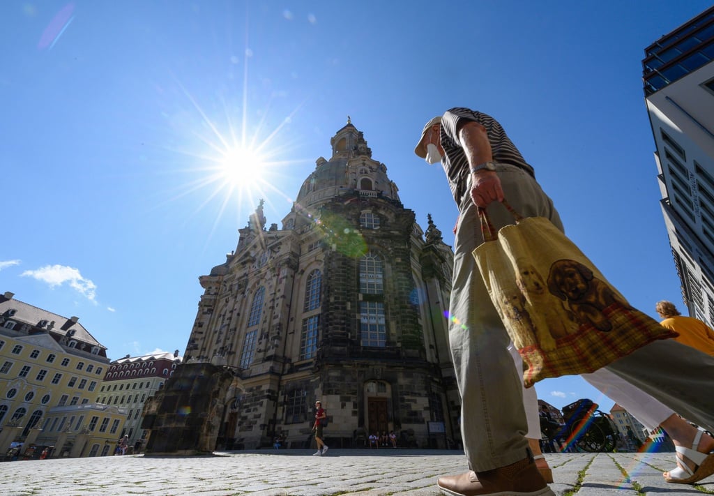 Menschen, die Masken tragen, laufen auf dem Neumarkt vor der Frauenkirche entlang.