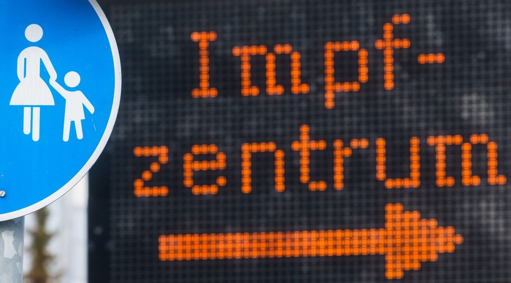 Eine elektronische Anzeigetafel mit dem Wort „Impfzentrum“ hinter einem Verkehrsschild „Sonderweg Fußgänger“ weist den Weg zu einem Impfzentrum.