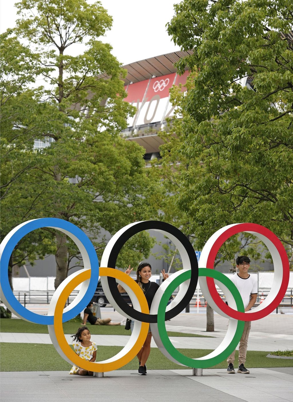 Menschen stehen stehen hinter den Olympischen Ringen in Tokio.