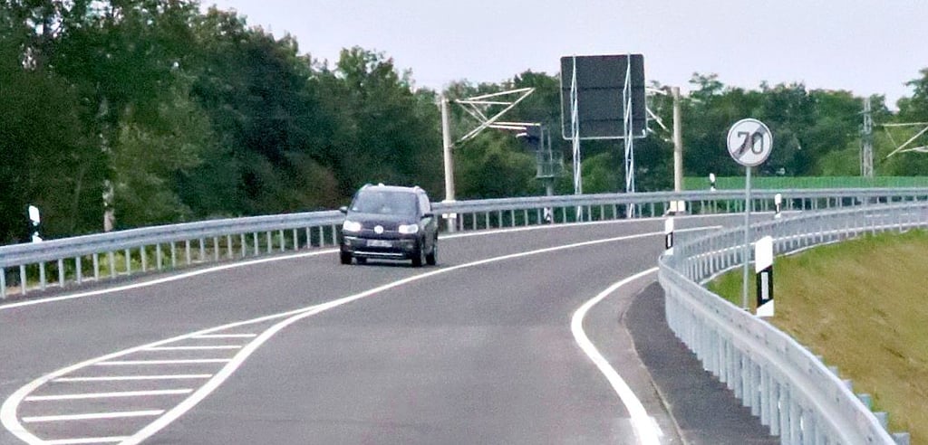 Entlang der Umgehung sind Fahrbahnbeplankungen mit Gummimatten ummantelt (rechts dunkle Fläche vor Planke). Das soll den Bewuchs der Schutzbarrieren mit Gräsern verhindern.