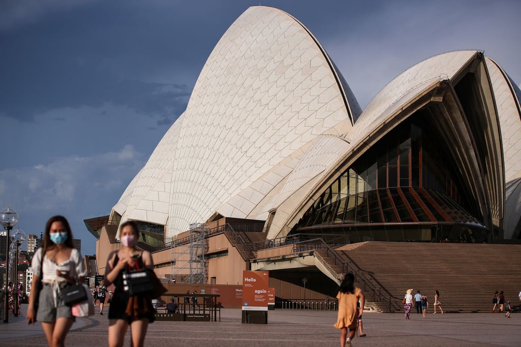 Passanten mit Mund-Nasen-Bedeckung gehen am berühmten Opernhaus in Sydney vorbei.